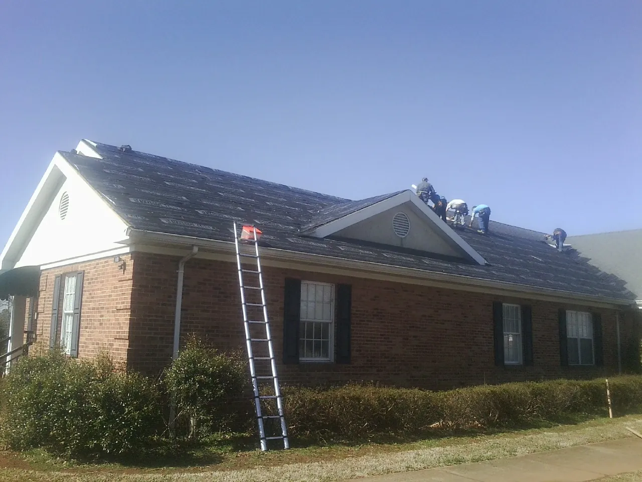Crew tearing shingles off a brick ranch roof with a ladder set — Emergency Roof Repair work by our crew in Inglis