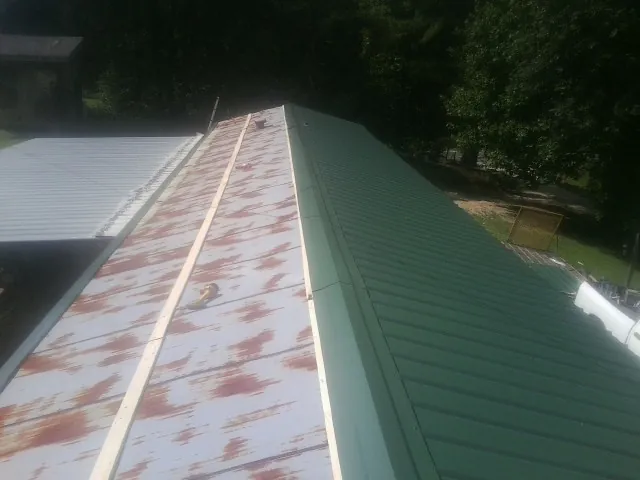 Old rusted panels beside newly installed green metal roofing — Wind Damage Roof Repair by Roofing Brothers in Inglis