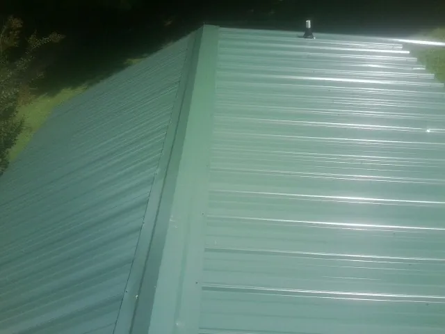 New green metal panels meeting at the ridge of a roof — Flat Roof Repair work by our crew in Inglis
