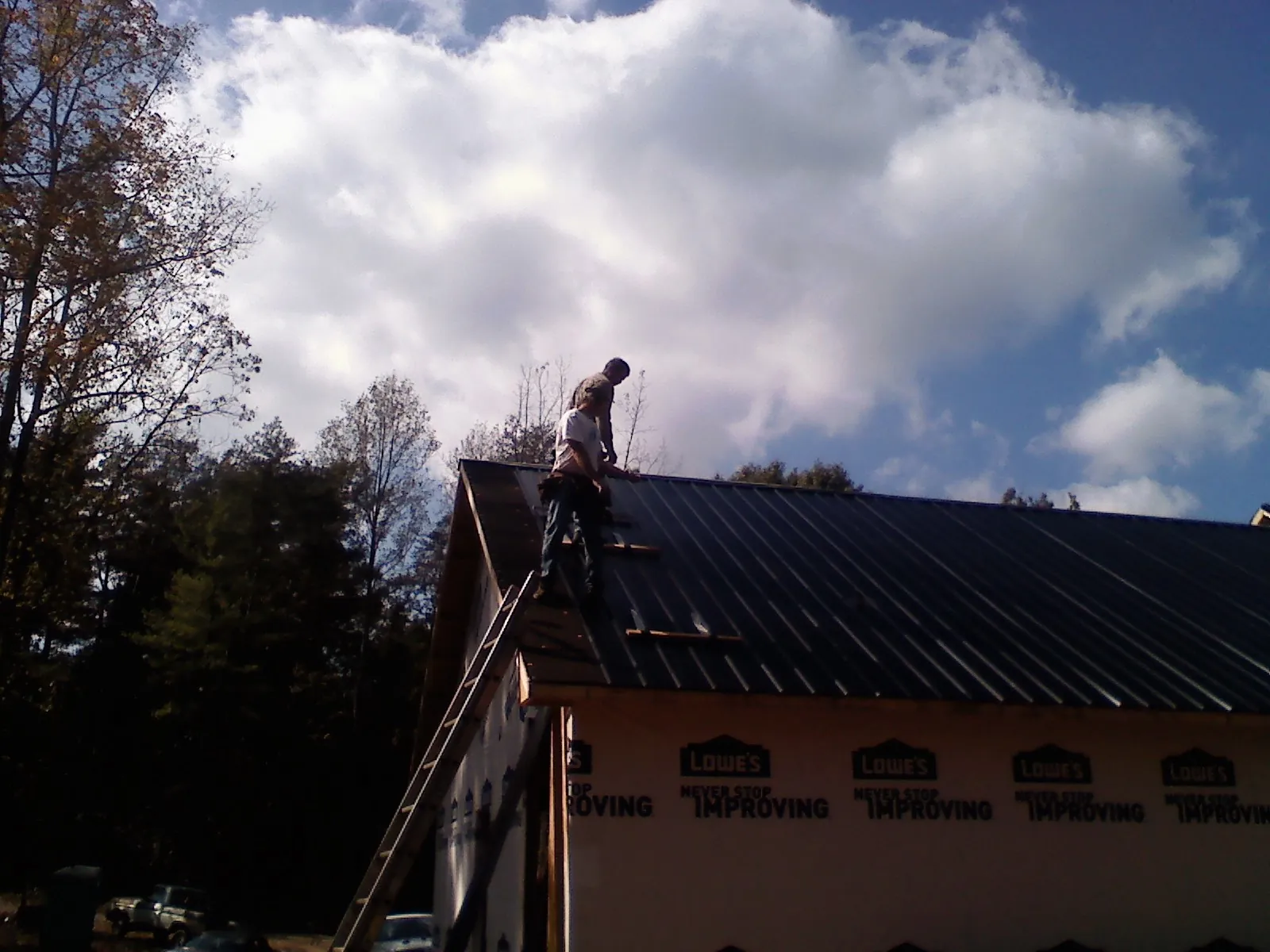 Roofer fastening dark metal panels high against a cloudy sky, from a Roof Inspection job in Inglis