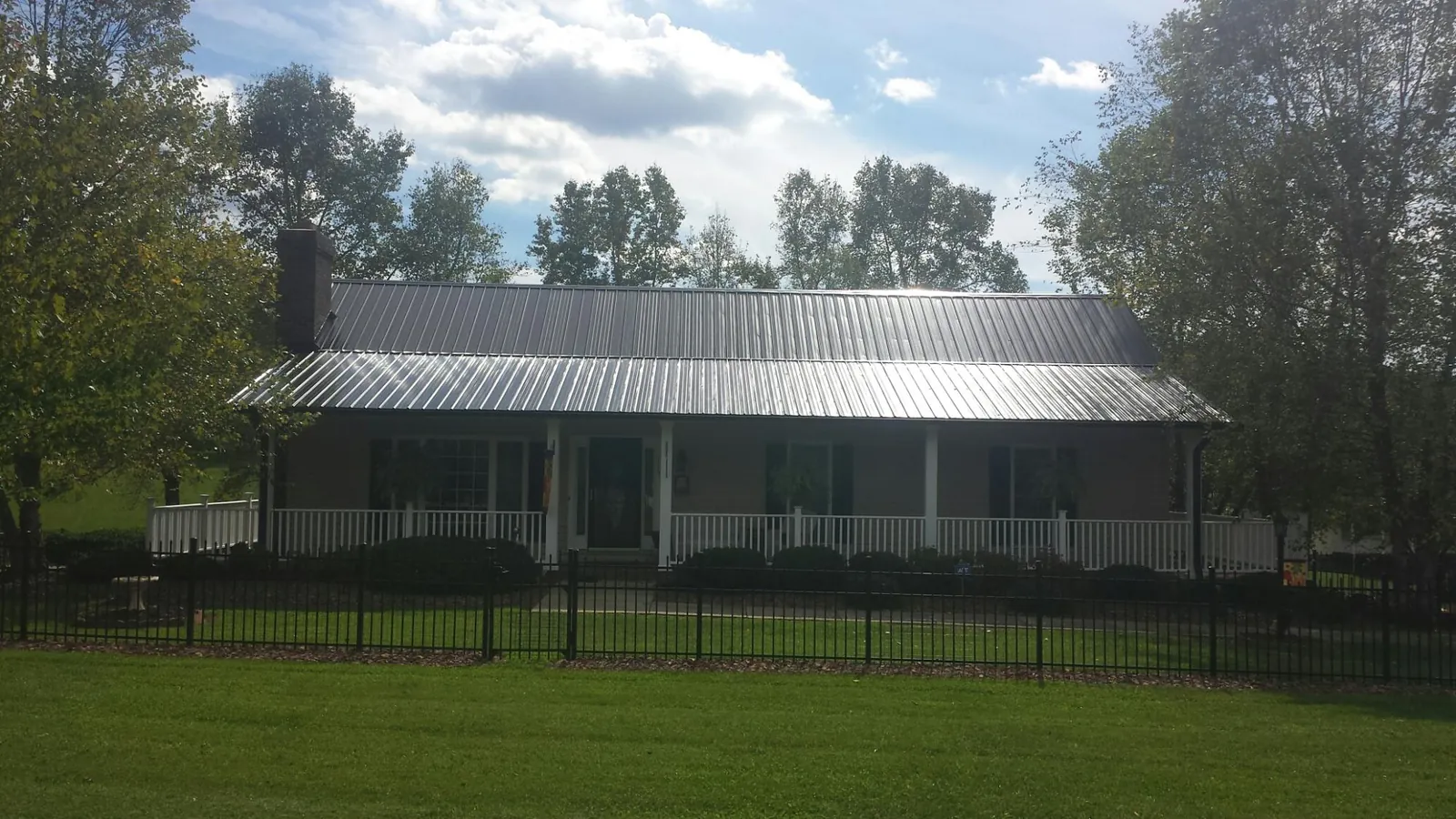Gray metal roof on a brick ranch with a full width front porch — Gutter Guard Installation work by our crew in Inglis