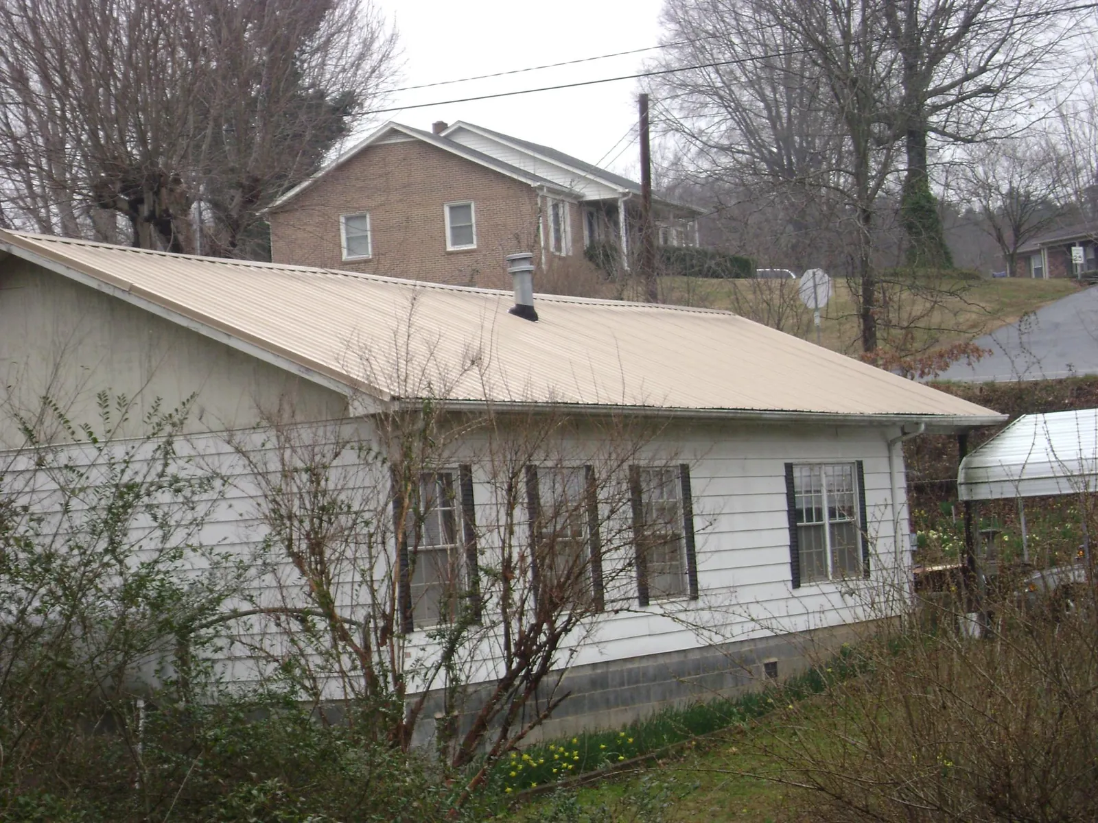 Tan metal roof on a white sided house set into a hillside — Commercial Roofing by Roofing Brothers in Inglis